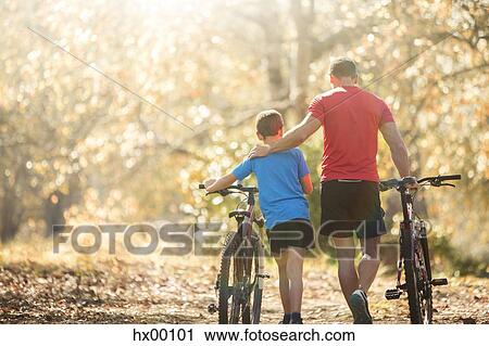 Affectionate father and son walking mountain bikes on path in woods View Large Photo Image Stock Image - Affectionate father and son walking mountain bikes on path in woods. Fotosearch