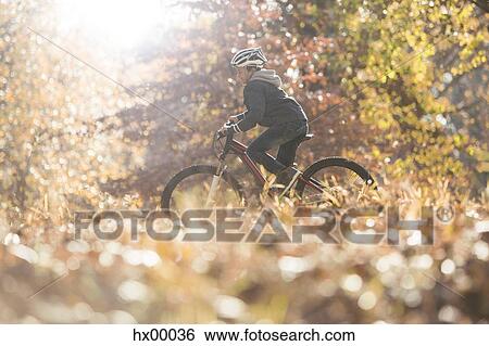 Stock Photograph - Boy bike riding in woods with autumn leaves. Fotosearch