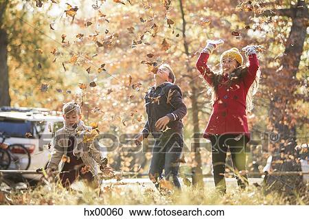 Stock Image - Boys and girl throwing autumn leaves overhead. Fotosearch