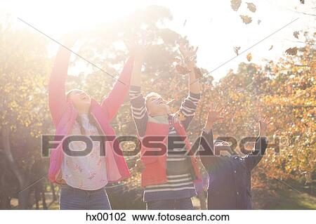 Stock Image - Boys and girl throwing autumn leaves overhead. Fotosearch