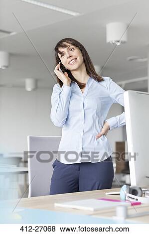 Brunette businesswoman talking on cell phone at desk in office View Large Photo Image Stock Photo - Brunette businesswoman talking on cell phone at desk in office. Fotosearch