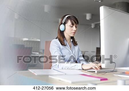 Stock Photograph - Brunette businesswoman with headphones working at computer in office. Fotosearch