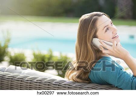 Stock Photo - Brunette woman talking on cell phone at poolside. Fotosearch