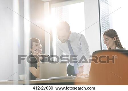 Business people working at laptop in sunny conference room meeting View Large Photo Image Stock Image - Business people working at laptop in sunny conference room meeting. Fotosearch