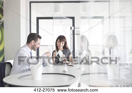 Stock Photography - Businessman and businesswoman eating Chinese takeout food in office cafeteria. Fotosearch