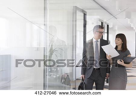 Stock Photograph - Businessman and businesswoman discussing report in office corridor. Fotosearch