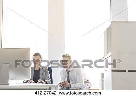 Businessman and businesswoman working at computer in sunny office View Large Photo Image Stock Image - Businessman and businesswoman working at computer in sunny office. Fotosearch
