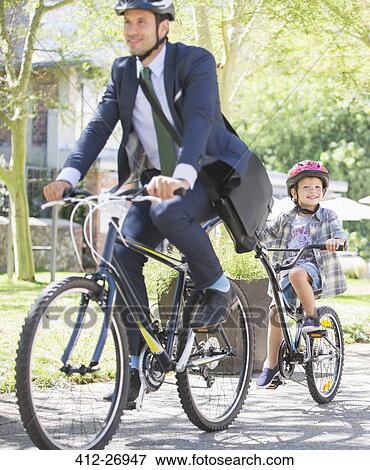 Businessman in suit and helmet riding tandem bicycle with son View Large Photo Image Stock Photo - Businessman in suit and helmet riding tandem bicycle with son. Fotosearch
