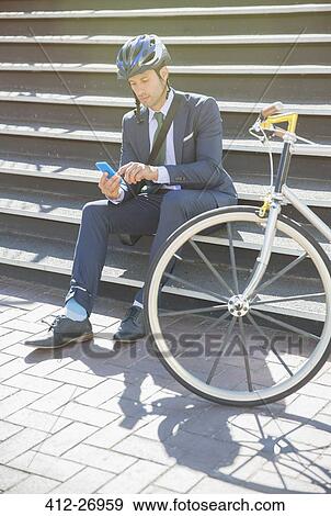 Businessman in suit and helmet texting with cell phone next to bicycle on sunny urban stairs View Large Photo Image Stock Photo - Businessman in suit and helmet texting with cell phone next to bicycle on sunny urban stairs. Fotosearch
