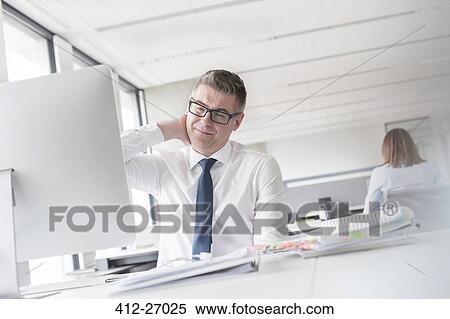 Businessman rubbing neck at computer in office View Large Photo Image Stock Photography - Businessman rubbing neck at computer in office. Fotosearch
