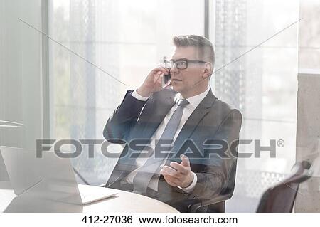 Stock Photograph - Businessman talking on cell phone gesturing in office. Fotosearch