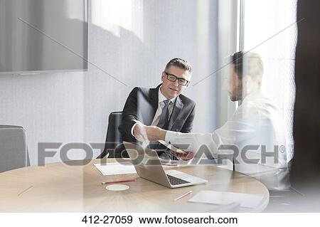 Businessmen discussing paperwork at laptop in conference room View Large Photo Image Stock Photo - Businessmen discussing paperwork at laptop in conference room. Fotosearch