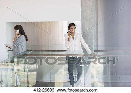 Stock Image - Businesswoman talking on cell phone in office. Fotosearch