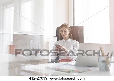 Businesswoman texting with cell phone in sunny office View Large Photo Image Stock Photo - Businesswoman texting with cell phone in sunny office. Fotosearch