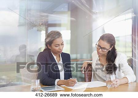Stock Photo - Businesswomen reviewing paperwork in conference room. Fotosearch