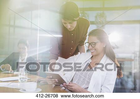 Businesswomen using digital tablet in sunny conference room View Large Photo Image Stock Photo - Businesswomen using digital tablet in sunny conference room. Fotosearch
