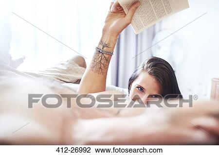 Stock Image - Casual couple laying on bed reading book. Fotosearch