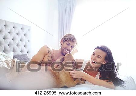 Casual couple petting dog on bed View Large Photo Image Stock Photography - Casual couple petting dog on bed. Fotosearch