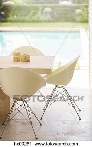 Stock Image - Chairs around table at poolside. Fotosearch