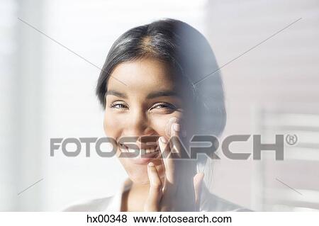 Stock Photo - Close up portrait smiling woman applying moisturizer to cheek. Fotosearch