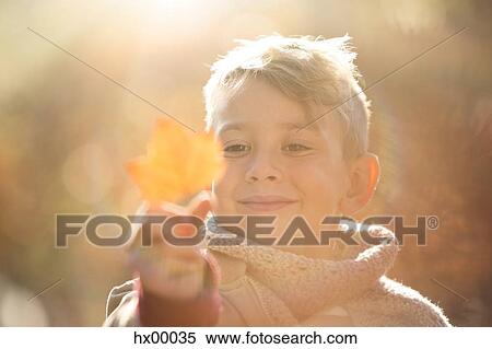 Stock Photography - Close up smiling boy holding golden autumn leaf. Fotosearch