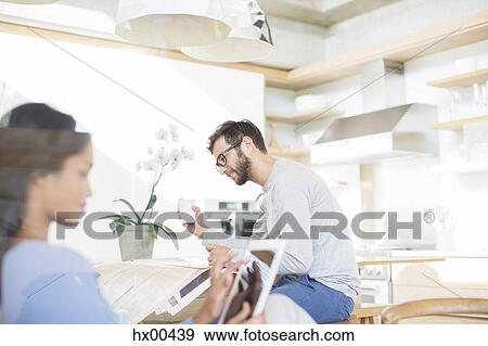 Couple drinking coffee, reading newspaper and using digital tablet in kitchen View Large Photo Image Stock Photo - Couple drinking coffee, reading newspaper and using digital tablet in kitchen. Fotosearch
