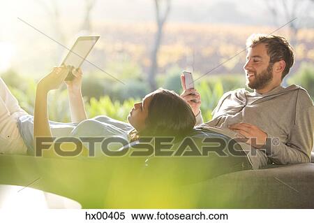 Stock Photography - Couple laying and using digital tablet and cell phone on sunny patio. Fotosearch