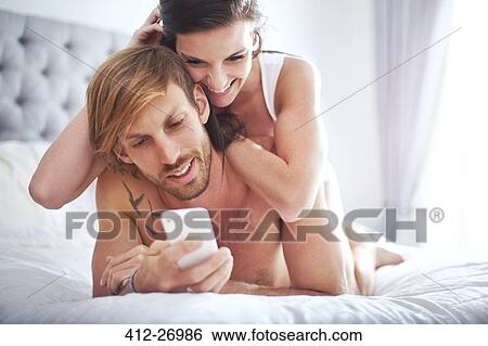 Couple laying on bed texting with cell phone View Large Photo Image Stock Photograph - Couple laying on bed texting with cell phone. Fotosearch