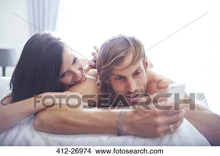Couple relaxing on bed texting with cell phone View Large Photo Image Picture - Couple relaxing on bed texting with cell phone. Fotosearch