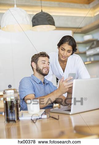 Stock Photo - Couple texting with cell phone at laptop. Fotosearch