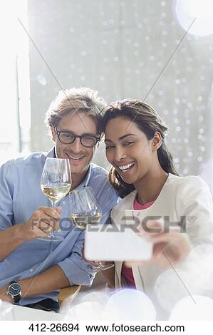 Picture - Couple with white wine taking selfie with camera phone. Fotosearch
