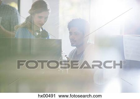 Stock Image - Creative business people with headphones using computer in sunny office. Fotosearch