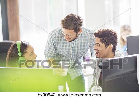 Stock Image - Creative business people with headphones and coffee laughing at computers. Fotosearch