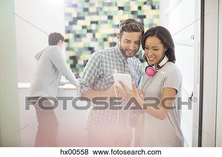 Stock Photo - Creative business people with headphones using digital tablet in office. Fotosearch