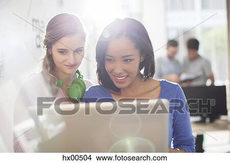 Picture - Creative businesswomen with headphones using digital tablet. Fotosearch