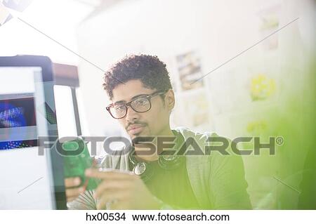 Picture - Creative designer with headphones examining part in office. Fotosearch