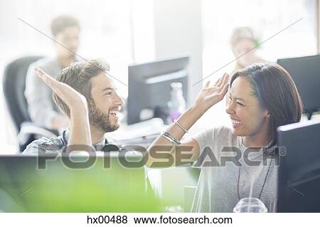 Stock Photo - Enthusiastic business people high fiving in office. Fotosearch