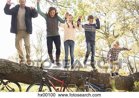 Stock Image - Enthusiastic family jumping from fallen log over bicycles. Fotosearch