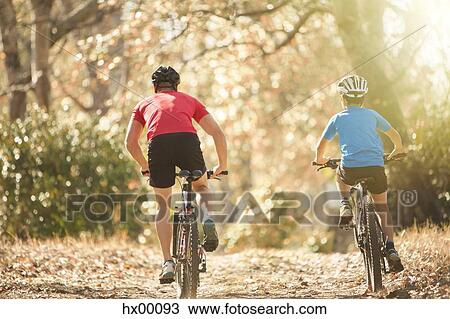 Stock Image - Father and son mountain biking on path in woods. Fotosearch