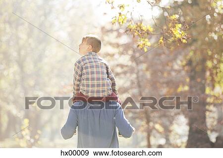 Stock Photo - Father carrying son on shoulders below autumn leaves. Fotosearch