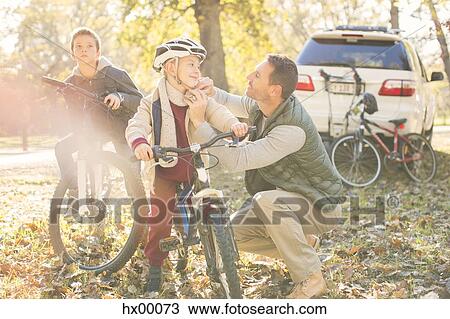 Father fastening helmet of son on bicycle in autumn woods View Large Photo Image Stock Image - Father fastening helmet of son on bicycle in autumn woods. Fotosearch