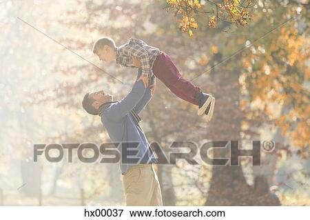 Stock Photo - Father lifting son overhead in woods with autumn leaves. Fotosearch