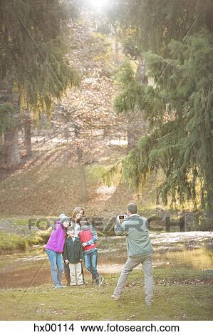 Picture - Father photographing family with camera phone in park. Fotosearch