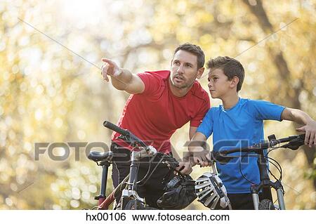Stock Photograph - Father pointing and explaining to son on mountain bikes. Fotosearch