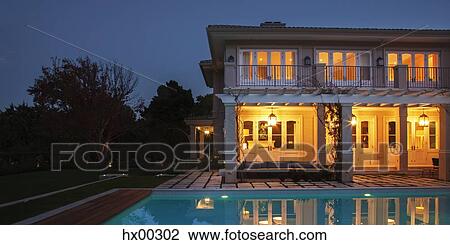Stock Image - Illuminated luxury house with swimming pool at night. Fotosearch