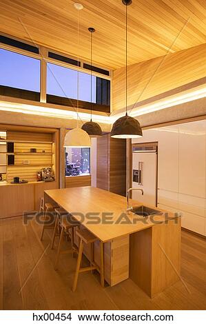 Illuminated slanted wood ceiling and pendant lights over kitchen island View Large Photo Image Picture - Illuminated slanted wood ceiling and pendant lights over kitchen island. Fotosearch