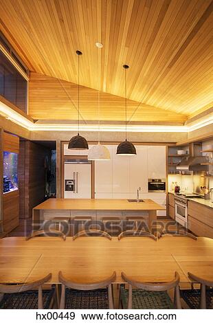 Stock Photo - Illuminated slanted wood ceiling over luxury kitchen and dining table. Fotosearch