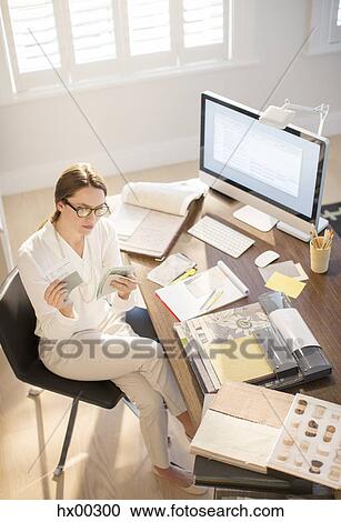 Stock Image - Interior designer examining swatches at desk in home office. Fotosearch