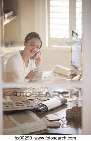 Stock Image - Interior designer examining swatches and talking on cell phone in home office. Fotosearch