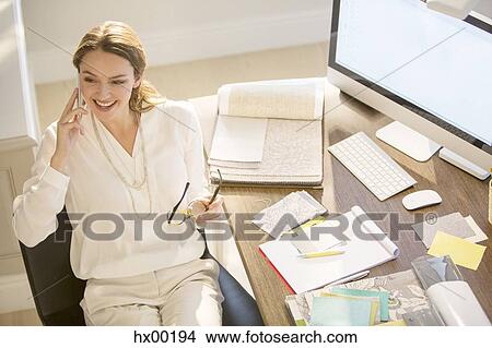 Picture - Interior designer talking on cell phone at desk. Fotosearch